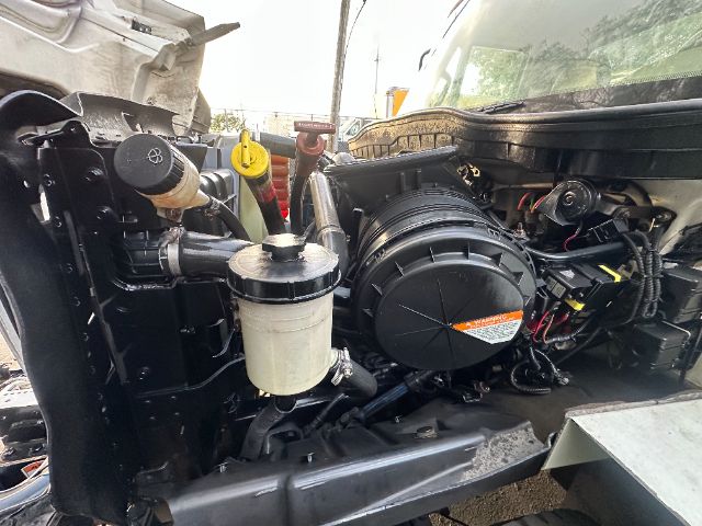 International 7400 vacuum truck engine bay showing heavy-duty radiator, air filter canister, and auxiliary fluid reservoir with hoses and wiring visible.