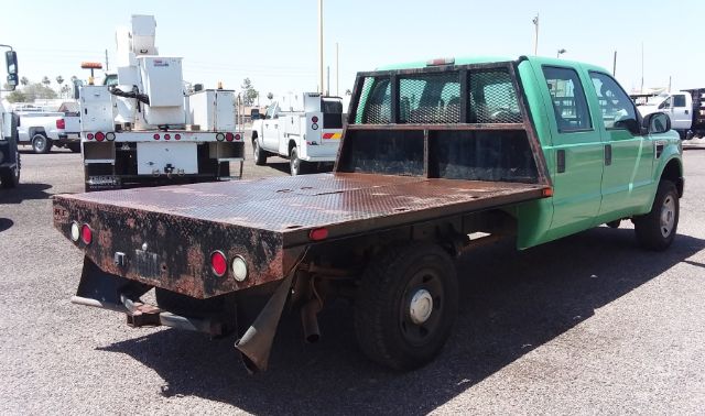 2009 Ford F250 4X4 crew cab flatbed with rusted steel flatbed and green cab, utility truck in a lot
