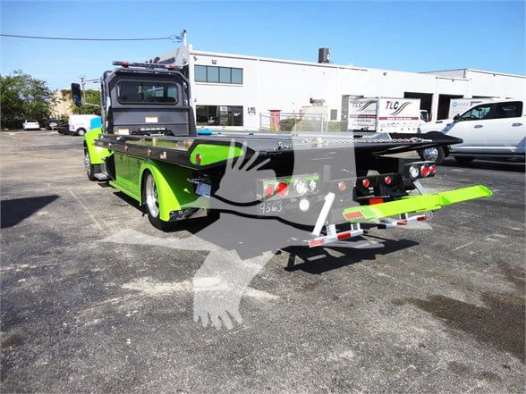 Green and black Peterbilt 337 flatbed tow truck with extended rear hitch and hydraulic controls, tail lights, and warning lights visible on back of bed.