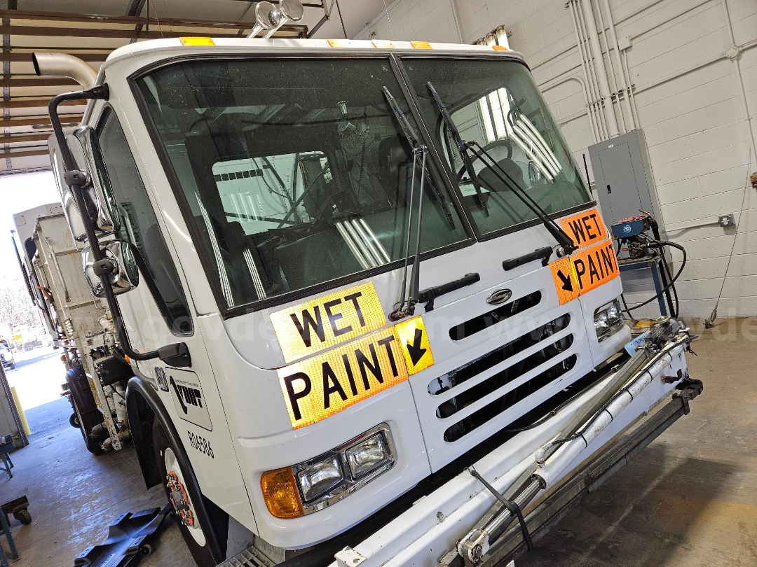 Front of a white 2003 Sterling M-B truck with large Wet Paint signs on the grille area, in a shop bay.