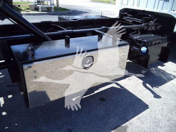 Truck bed fuel tank and chassis components under the cab of a 2015 Ford F650 XLT, with black painted metal toolbox and battery area visible.