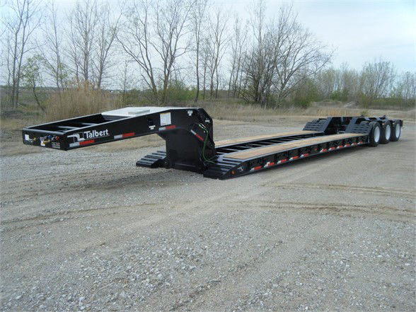 Talbert 55CC-HRG-T1 lowboy trailer in an outdoor yard showing long black main deck with wheel axles at rear and gooseneck hitch area.