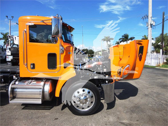 Orange Peterbilt 337 truck with raised cab showing interior components and side exhaust, front wheel and chrome steps visible.