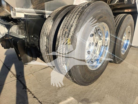 Trailer wheel assembly showing dual tandem axles with chrome rims and black tires, part of a dump trailer chassis.