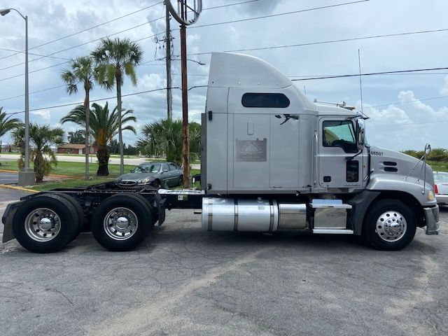 Side view of a 2010 Mack CXU613 conventional sleeper truck tractor in silver, showing cab with tall sleeper, fuel tanks, steps, and dual rear axles.