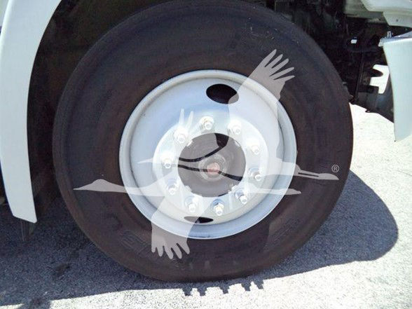 Wheel and tire on a truck visible with white rim and lug nuts; partial view of the fender and suspension.