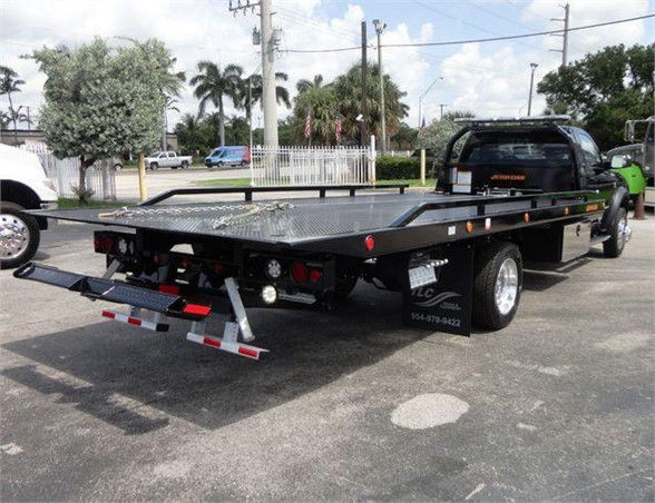 Flatbed tow truck with black steel bed and rear loading ramps, Ram 5500 SLT chassis visible, stock number J67261.