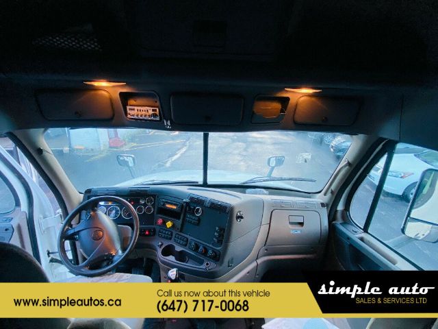 Cab interior of a 2012 Freightliner Cascadia truck showing dashboard, steering wheel, and overhead lights.