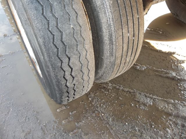 Two dual rear trailer tires on a Wilson flatbed trailer showing tread patterns and mud on the ground.