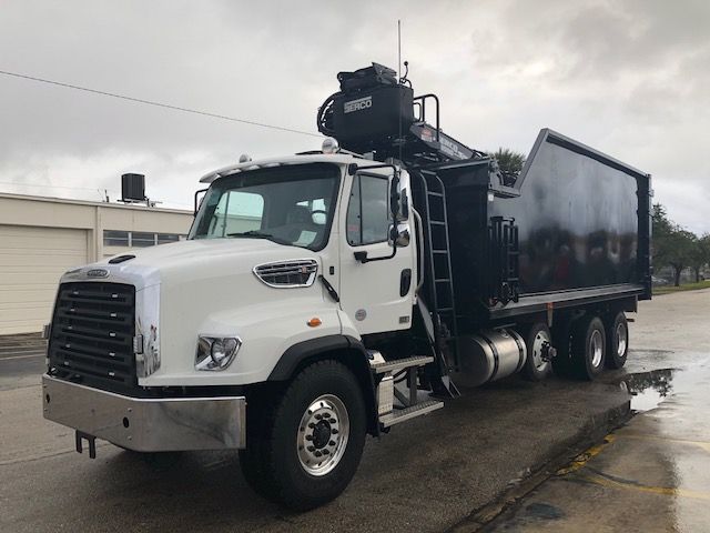 2019 Freightliner 114SD grapple truck with a mounted crane and dump bed, white cab, black dump body, on a wet pavement