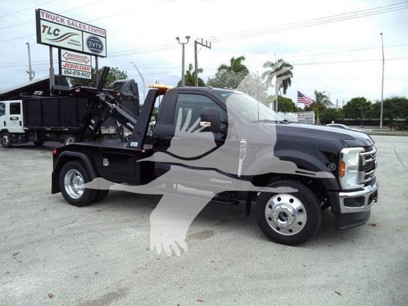 Ford F-450 tow truck with a heavy-duty hook lift, black cab and dual rear wheels, truck dealership in background