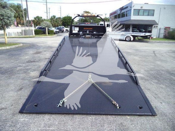 Truck bed of a 2023 Chevrolet Silverado 6500HD flatbed with metal diamond plate, towing chains, and a rear hitch, stock photo at a dealership.