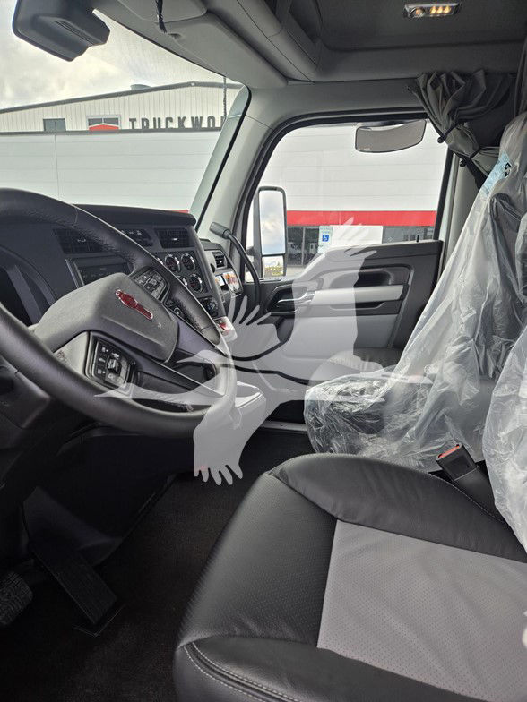 Interior of a new Kenworth T680 truck cab showing steering wheel, dashboard, center console, and plastic-covered driver seat with plastic seat cover