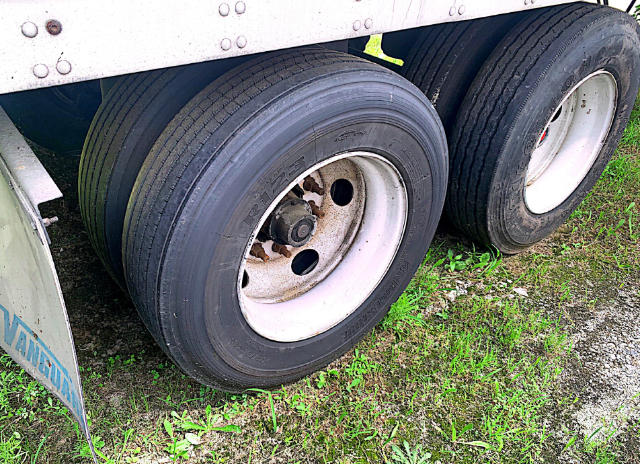 Dual rear trailer wheels with white rims and black tires under a metal trailer body.