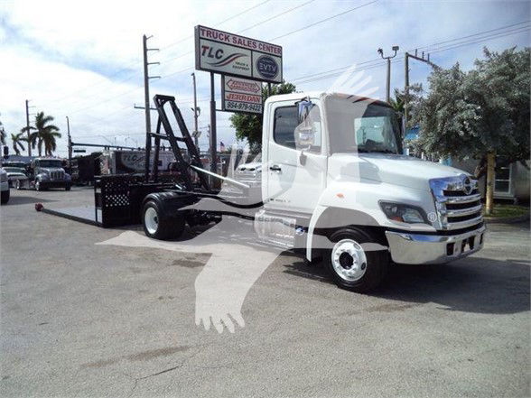 2017 Hino 258LP hooklift truck in a dealership lot with crane and open bed.