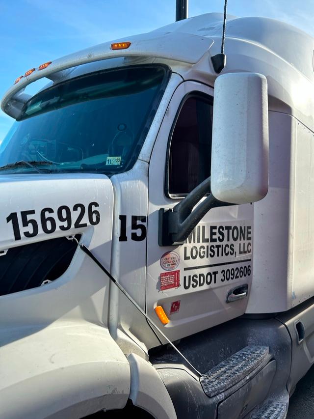 Truck cab of a Peterbilt 579 with Milestone Logistics LLC branding and USDOT number, showing side door decal and large white side mirror.