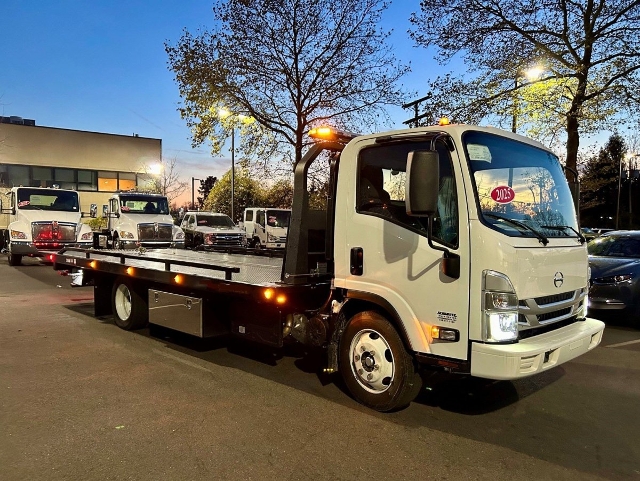 Tow truck with flatbed, white cab, side view showing deck and amber signal lights on roof.