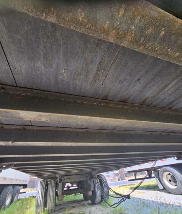 Trailer undercarriage showing wooden decking and frame with visible axles and wiring.