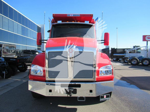 Kenworth T880 dump truck front view with red cab and chrome grille guard, dealer lot in background.