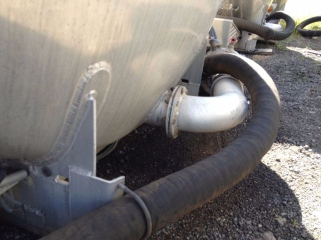 Truck vacuum tank with large black hose and metal piping; side view showing inlet/outlet connections and mounting brackets.