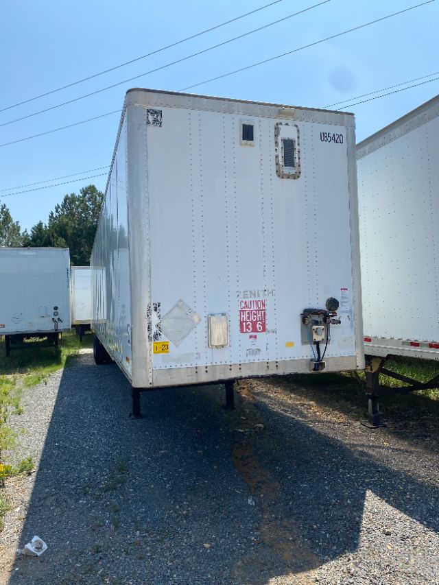 Trailer front view showing white Duraplate trailer with lift gate, with stickers and height warning, on support legs.