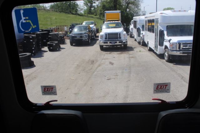 Bus interior rear view showing a parking lot with shuttle buses and a disabled access sign visible through rear window.