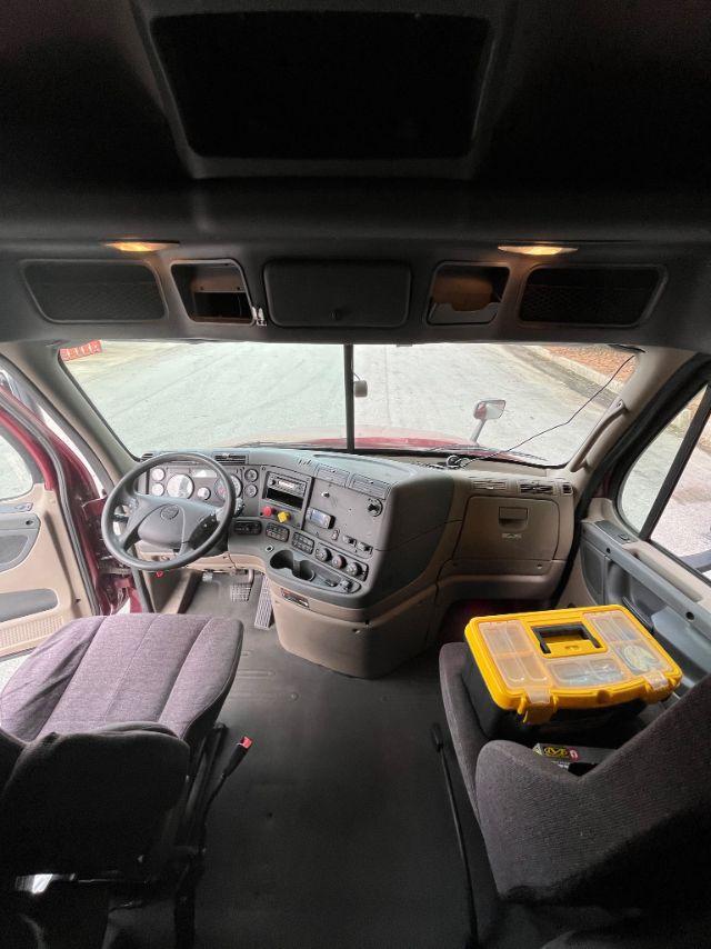 Cab interior of a Freightliner Cascadia truck showing dashboard, steering wheel, and a yellow tool case on the passenger seat.