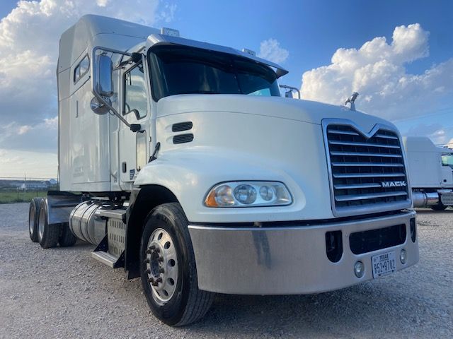 Mack CXU613 tractor with white cab and gray lower bumper, front grille, dual rear axles, and large side mirrors in a parking lot.
