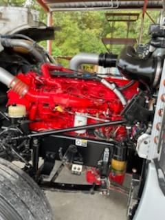 Peterbilt truck engine bay with bright red engine and various components; visible hoses, reservoirs, and mounts.