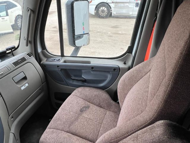 Truck cab interior of a 2017 Freightliner Cascadia showing brown cloth seat, dashboard, and side door panel.