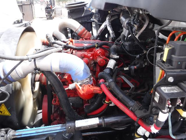 Engine bay of a 2018 International 4300 flatbed truck showing red engine components, hoses, and wiring.