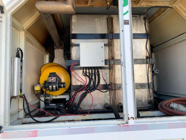 Trucks equipment bay with electrical harnesses, white metal junction box, and circular yellow device mounted on a frame inside a storage compartment.