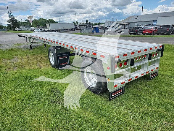 Flatbed trailer with tandem axle and metal decking, rear tailgate with rectangular cutouts, undercarriage and wheels visible on grassy lot.