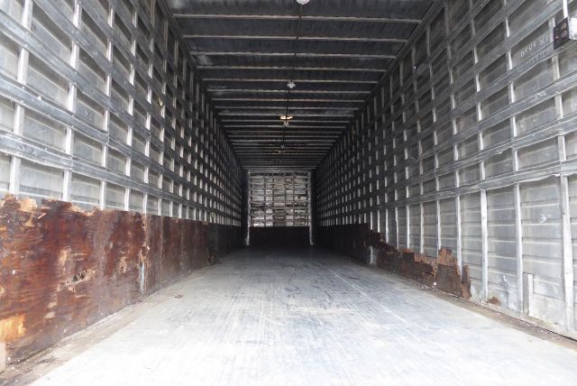 Trailer interior showing long cargo area with metal side walls and rust along lower panels. White door at far end. No visible branding or labels.