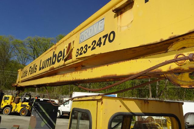 Grove RT58 crane boom with faded logo and contact number, yellow paint, utility truck cab visible below, trees in background.