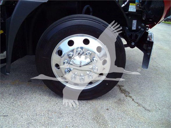 Wheel of a 2024 Mack MD6 tow truck showing polished steel rim with multiple circular holes and lug nuts.