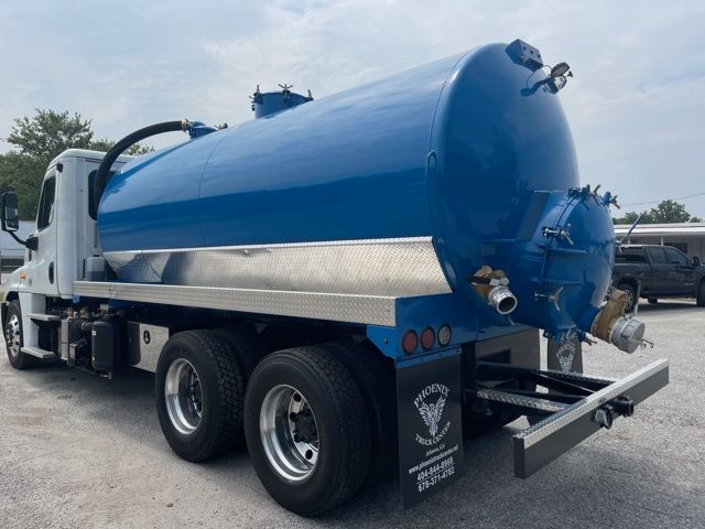 Truck-mounted vacuum tanker (blue) with cylindrical tank, rear plumbing and hoses, Freightliner Cascadia style cab visible,Dual rear wheels.