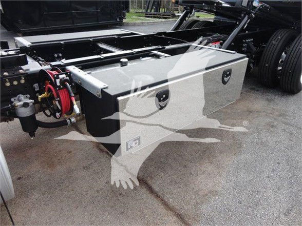 Two rectangular metal storage boxes mounted on a truck chassis with mounting latches, hoses, and a wheel visible in the background.
