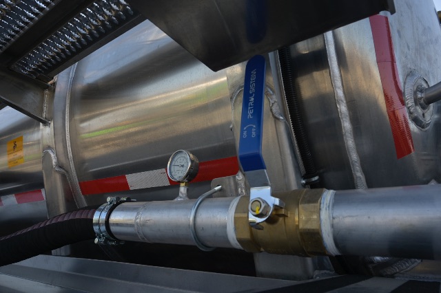 Vacuum trailer component with stainless tank, blue TETRA Systems valve lever, pressure gauge, and aluminum piping in view.