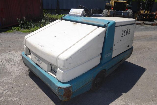 Truck-mounted Tennant ride-on floor scrubber with blue and white body, side number 2508, large rear white cover, on a gravel lot.