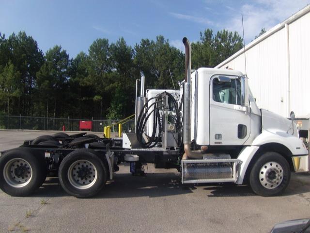 Side view of a white Freightliner Columbia conventional daycab truck chassis with dual rear axles and exposed exhaust stacks.