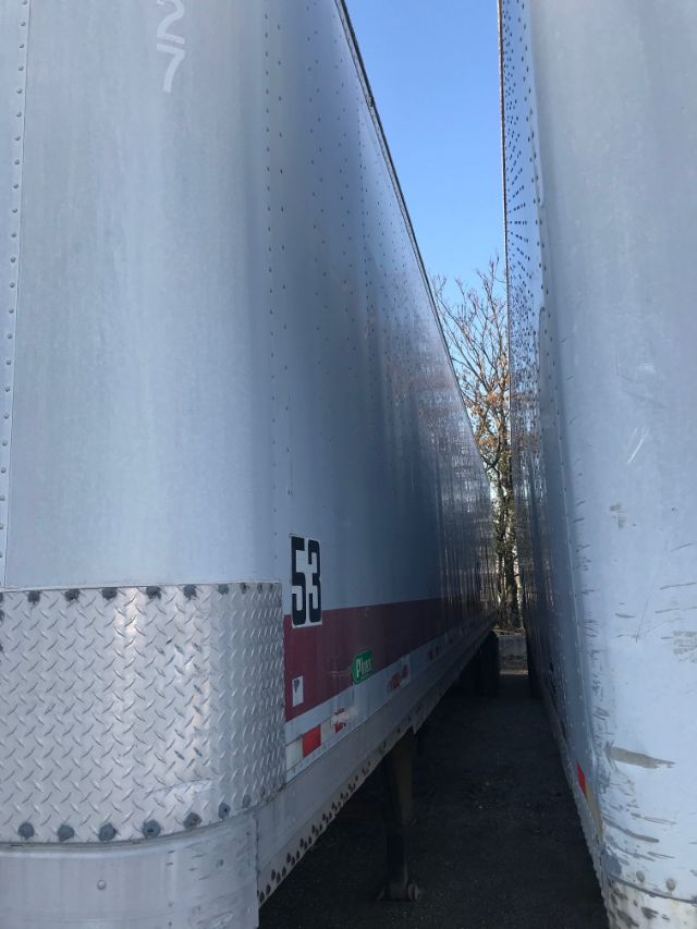 Trailer side showing number 53 with a red stripe and diamond plate front; two silver dry van trailers closely parked.