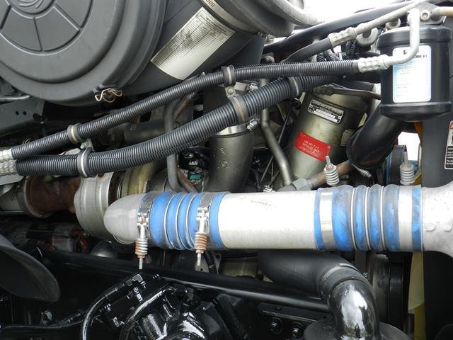 Freightliner engine bay showing blue silicone hose and metal piping along with various hoses, clamps, and a filter canister.