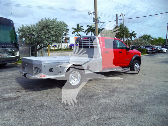 Ram 5500 flatbed tow truck in red cab with grey flatbed, showing utility compartments on the bed and dual rear wheels.