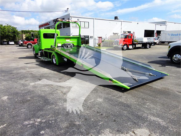 Green 2022 Peterbilt 337 tow truck with a lowered flatbed ramp in a dealership lot.