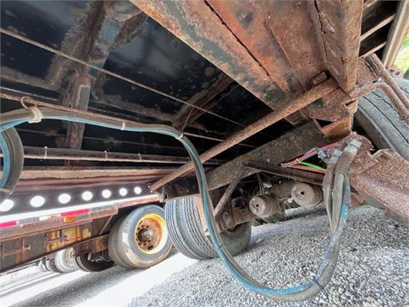 Underbody of a used Manac flatbed trailer showing rusty frame, wheel, suspension components, and hoses.