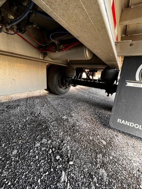Flatbed trailer underside showing wheel hub and suspension with rolling tarp mechanism nearby.