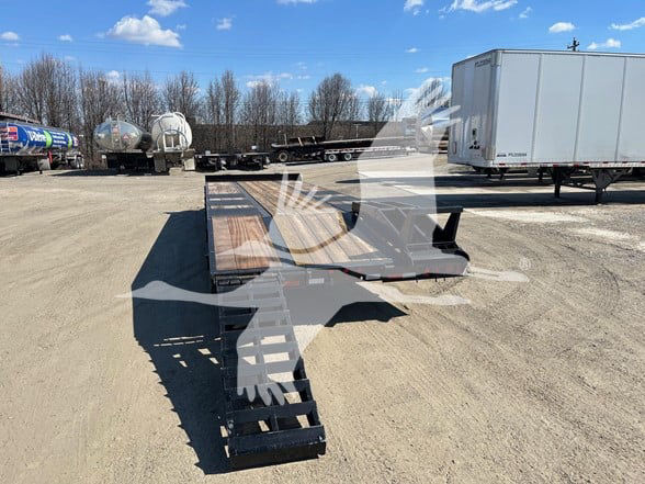 All-in-one trailer with a long flatbed and heavy-duty gooseneck, showing trailers and tanks in the background.