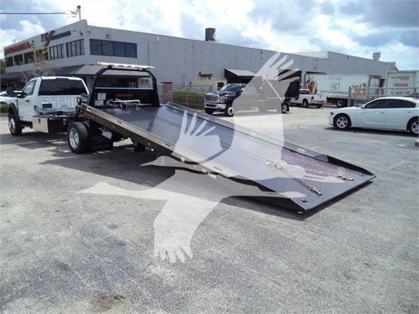 Ford F550 tow truck with a long flatbed ramp in a dealership lot; no legible labels or microtext visible on the equipment surface.