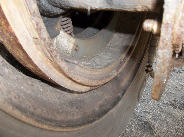 Wheel and rusty rim of a flatbed trailer wheel area showing tire and metal components.
